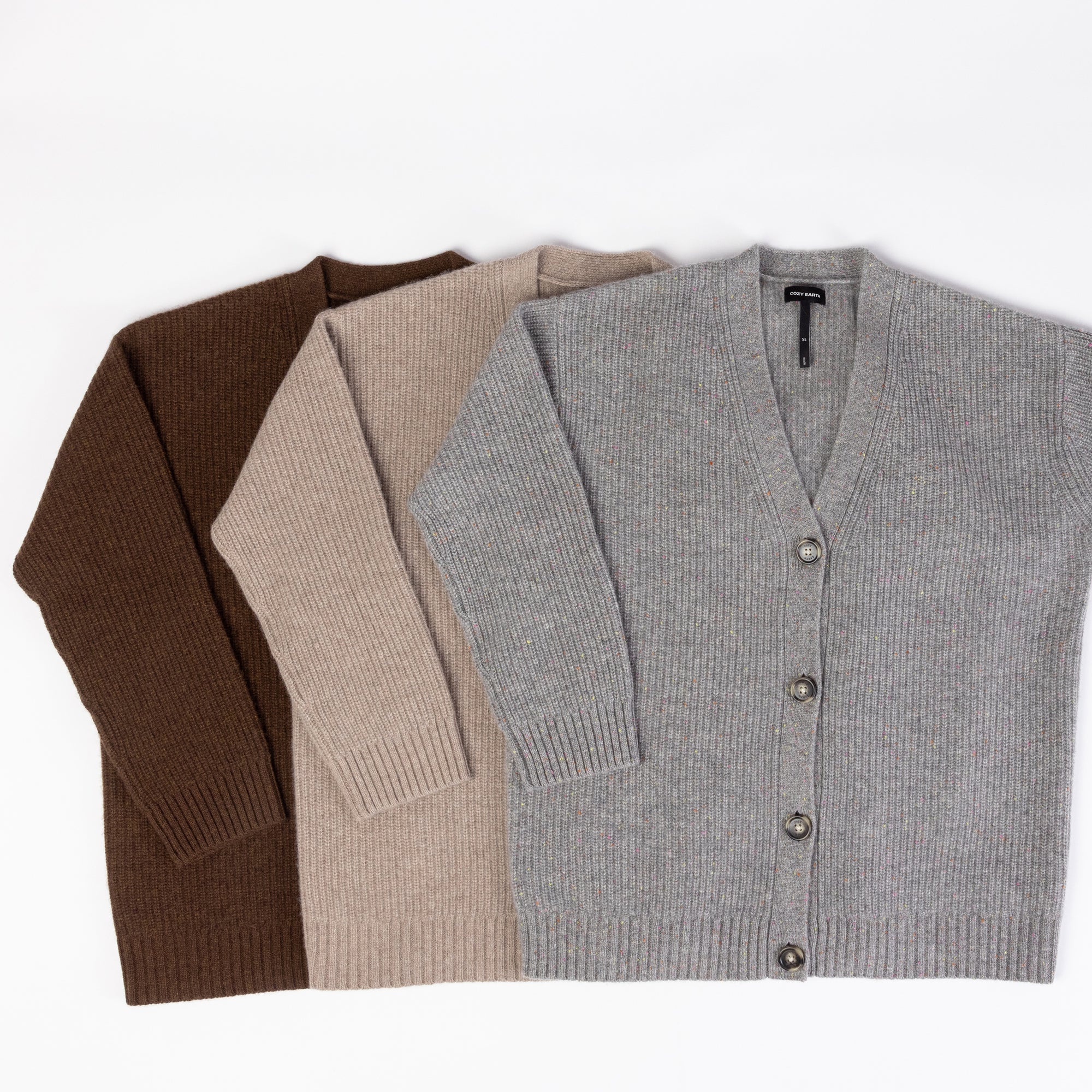 Three Oversized Sunday Cashmere Cardigans by Cozy Earth in brown, beige, and gray are laid flat on a white surface. Each cardigan features a V-neck and button-up front. 