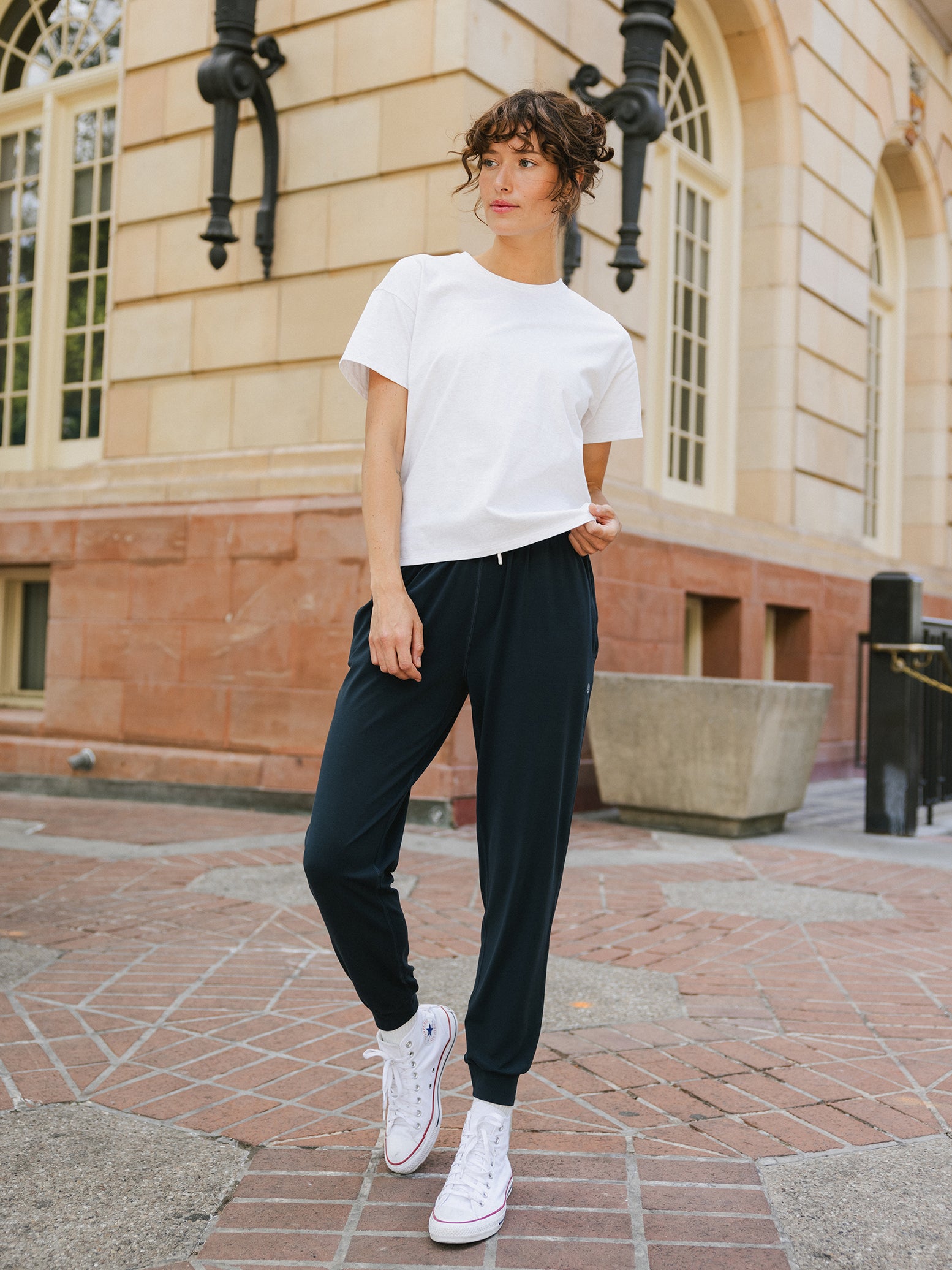 Woman on city sidewalk wearing white tee and black joggers 