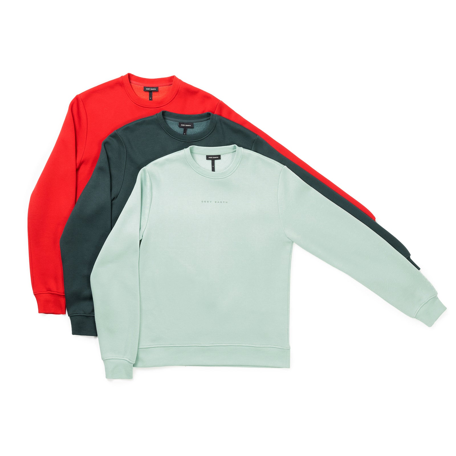 The display features three Men's CityScape Crewneck sweatshirts from Cozy Earth, each showcased in light green, dark green, and red. Their simple design is free from visible patterns, with sleeves extended to the side against a white background. 