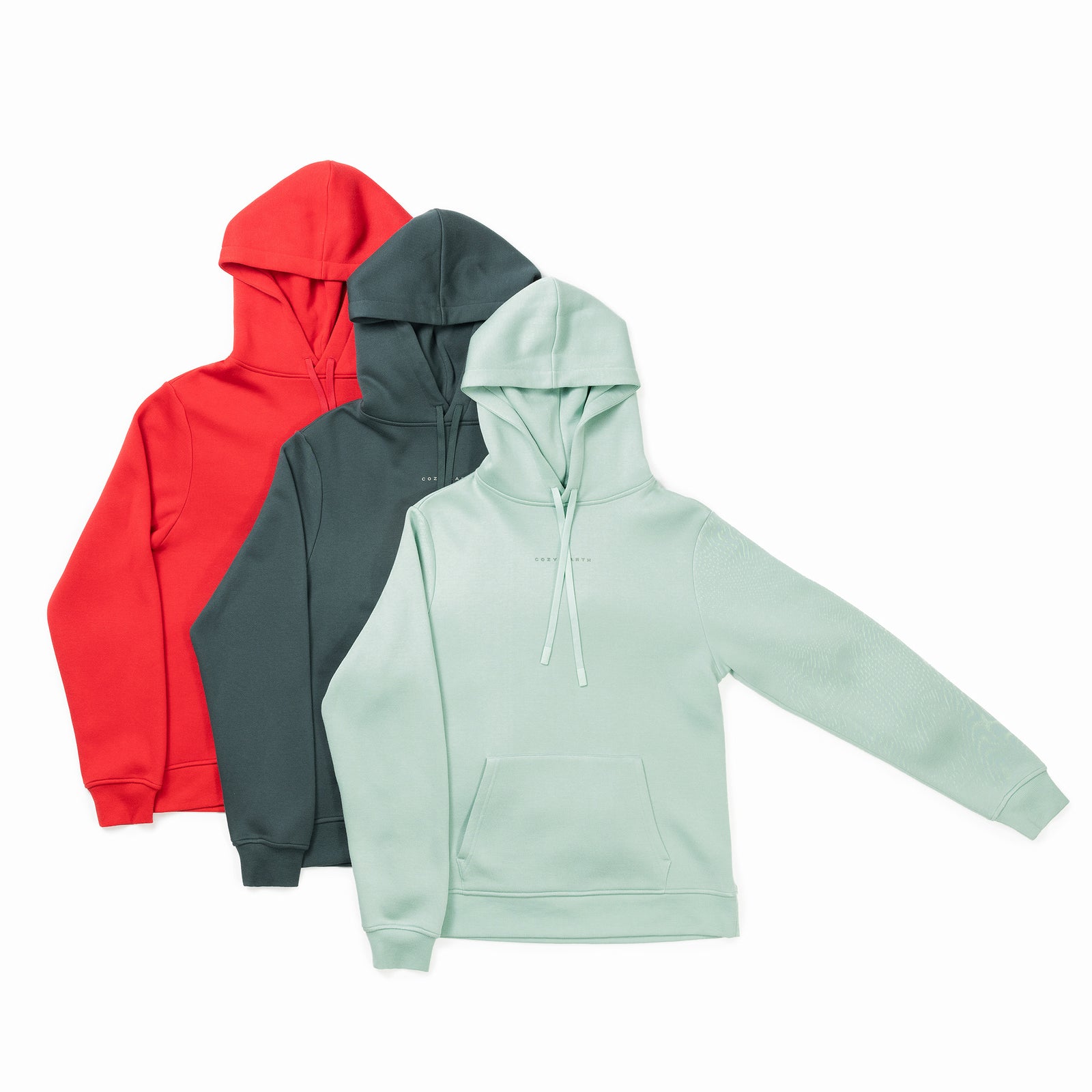 Displayed in the scene are three Cozy Earth Men's CityScape Hoodies, arranged with a light green hoodie at the forefront, a dark green one in the center, and a red one towards the back. Each hoodie is designed with a front pocket and drawstrings, and they slightly overlap each other. 