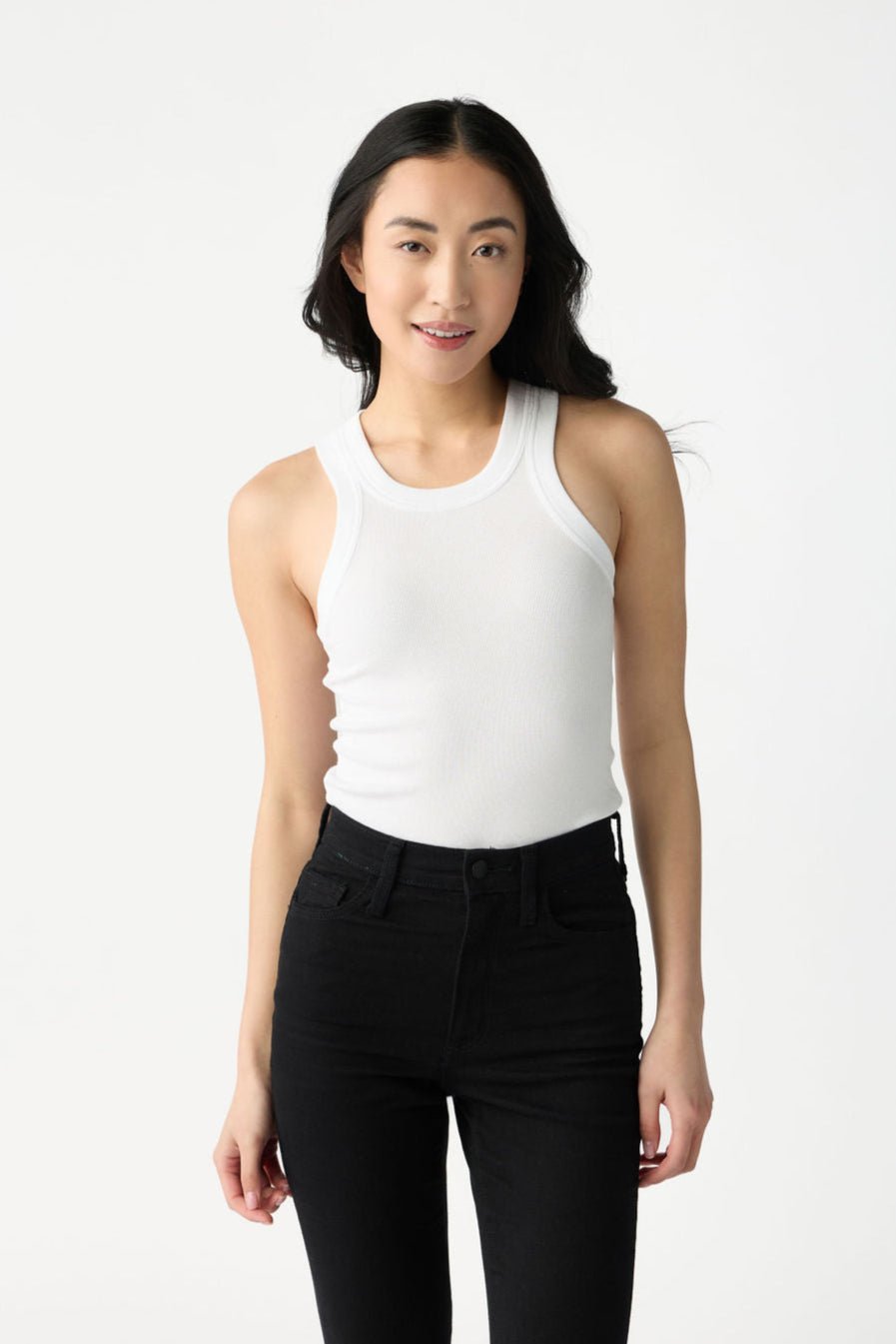 A dark haired woman wears Cozy Earth Women's Fine Ribbed Tank in White. She wears black jeans and stands in front of a white background. 