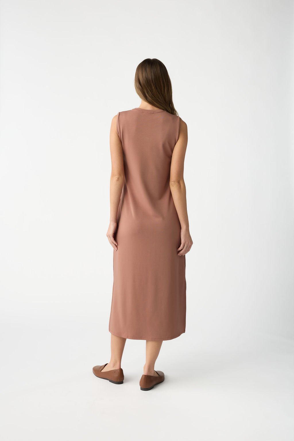 A woman with long brown hair, wearing the Women's Brushed Bamboo Sleeveless Midi Dress by Cozy Earth, stands against a plain white background in tan ankle-length attire and brown slip-on shoes. |Color:Saddle