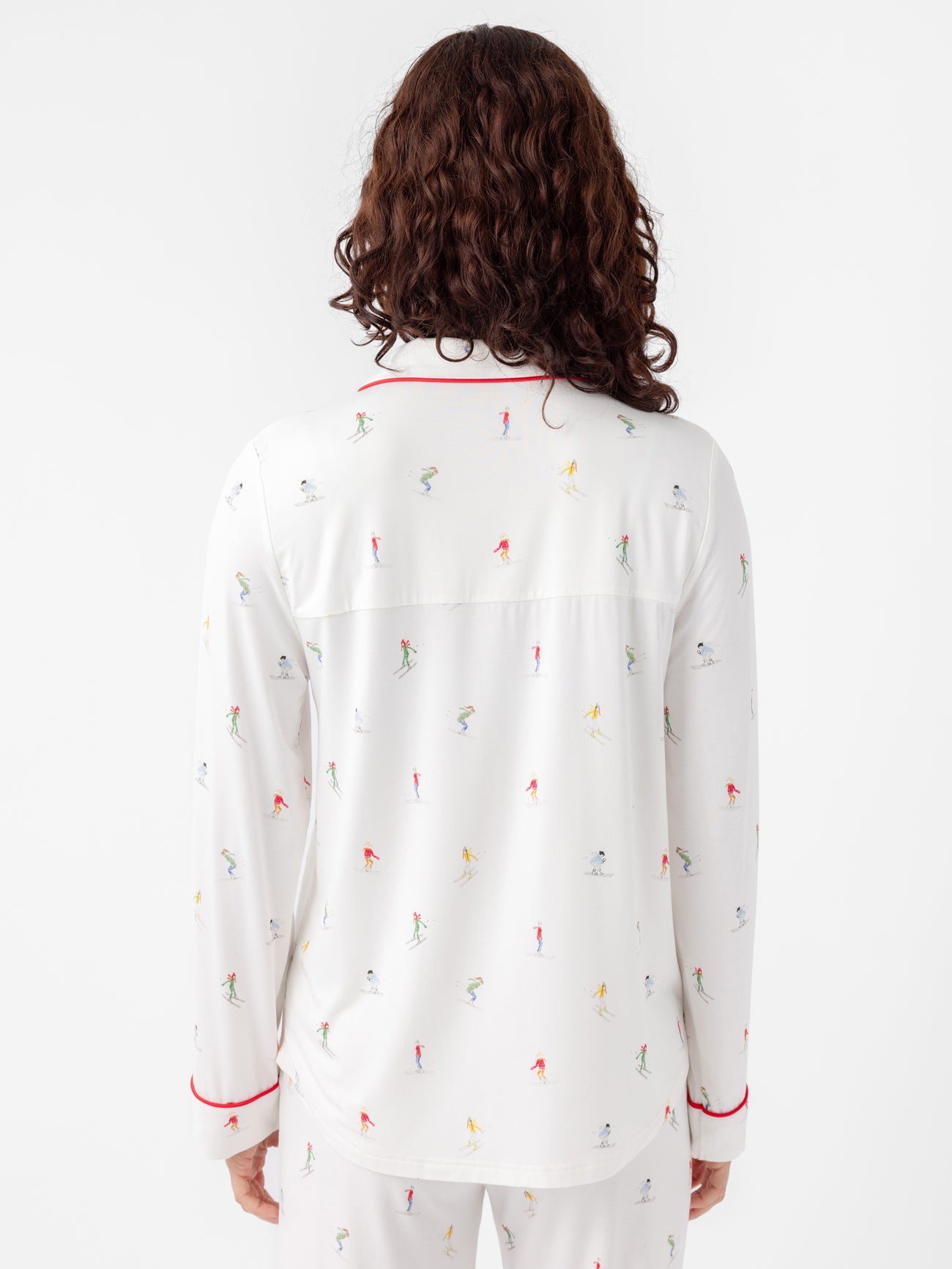 Rear view of a person with long, curly hair wearing Cozy Earth's Last Chance Women's Bamboo Stretch-Knit Long Sleeve Pajama Set. The sleepwear features colorful skier prints and red piping on the collar and cuffs against a plain white background. 