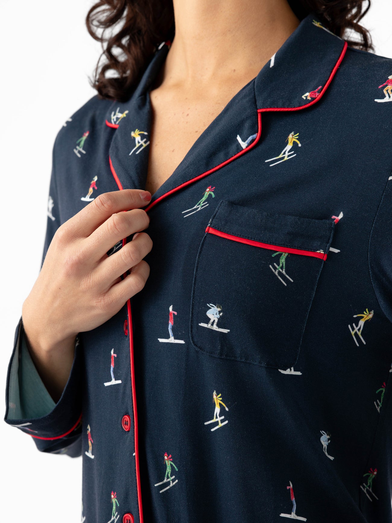 A person adjusts the collar of a Cozy Earth's Last Chance Women's Bamboo Stretch-Knit Long Sleeve Pajama Top, featuring a skiing print with red piping and buttons. 