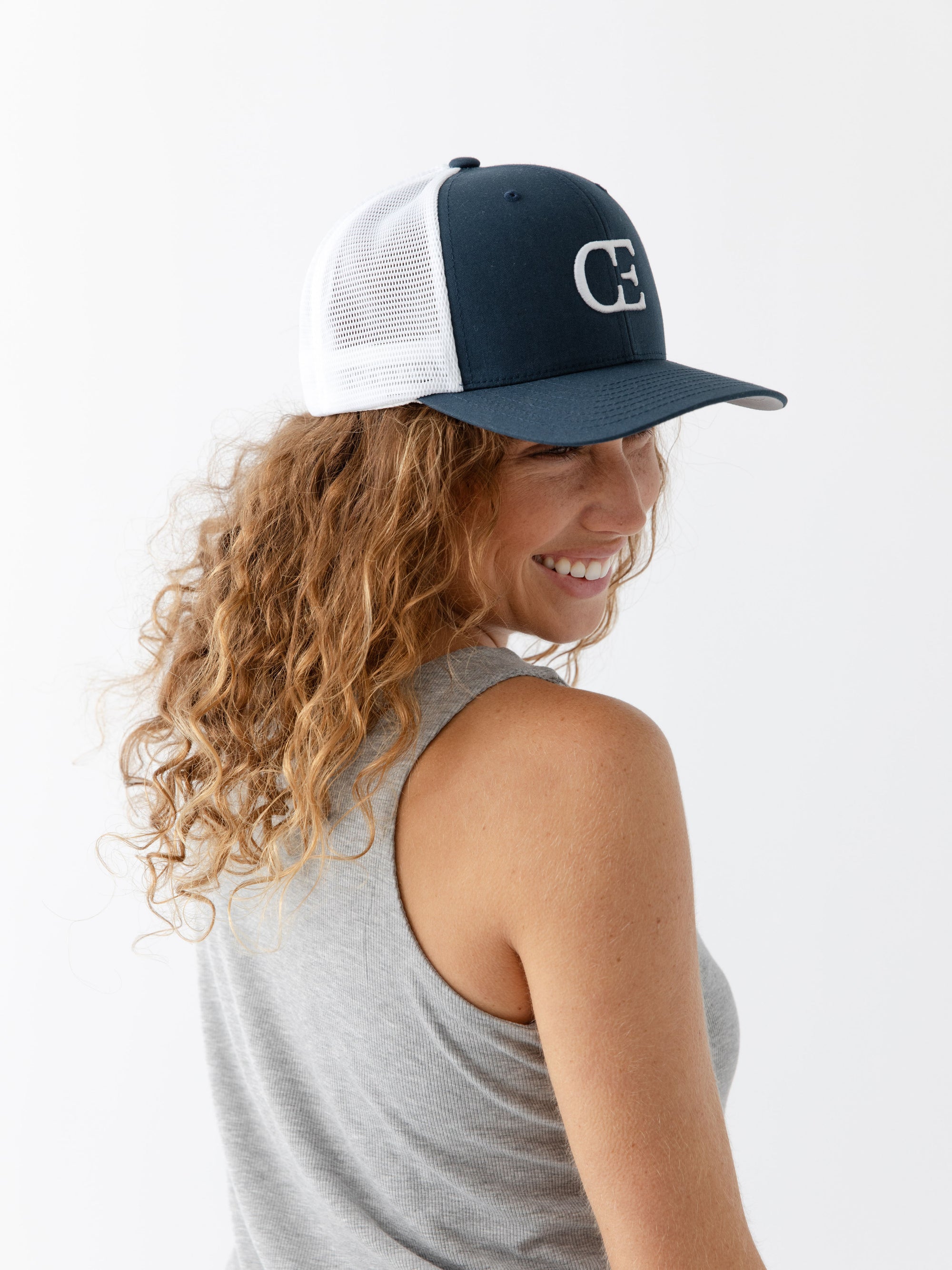 Woman wearing a Navy and white cap with a CE logo on a light gray background 