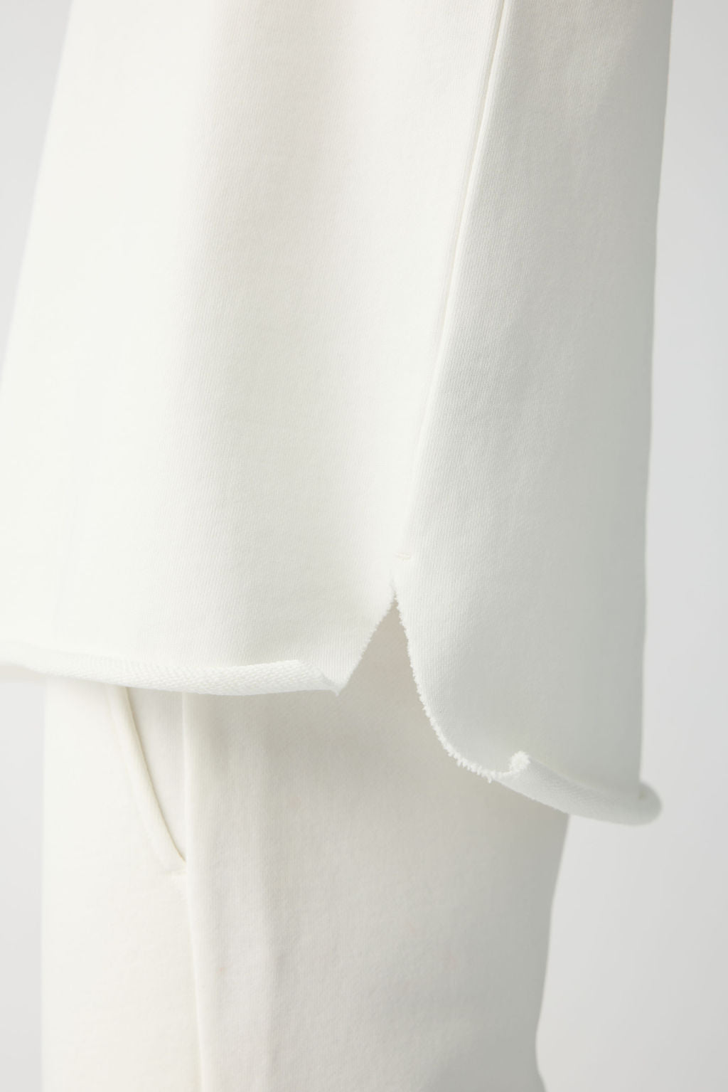 Close-up of a person in the Women's Chelsea Set by Cozy Earth. The side view shows a long white top with a subtle hem slit, paired with white pants. The fabric looks soft and smooth, offering a minimalist, elegant appearance. 