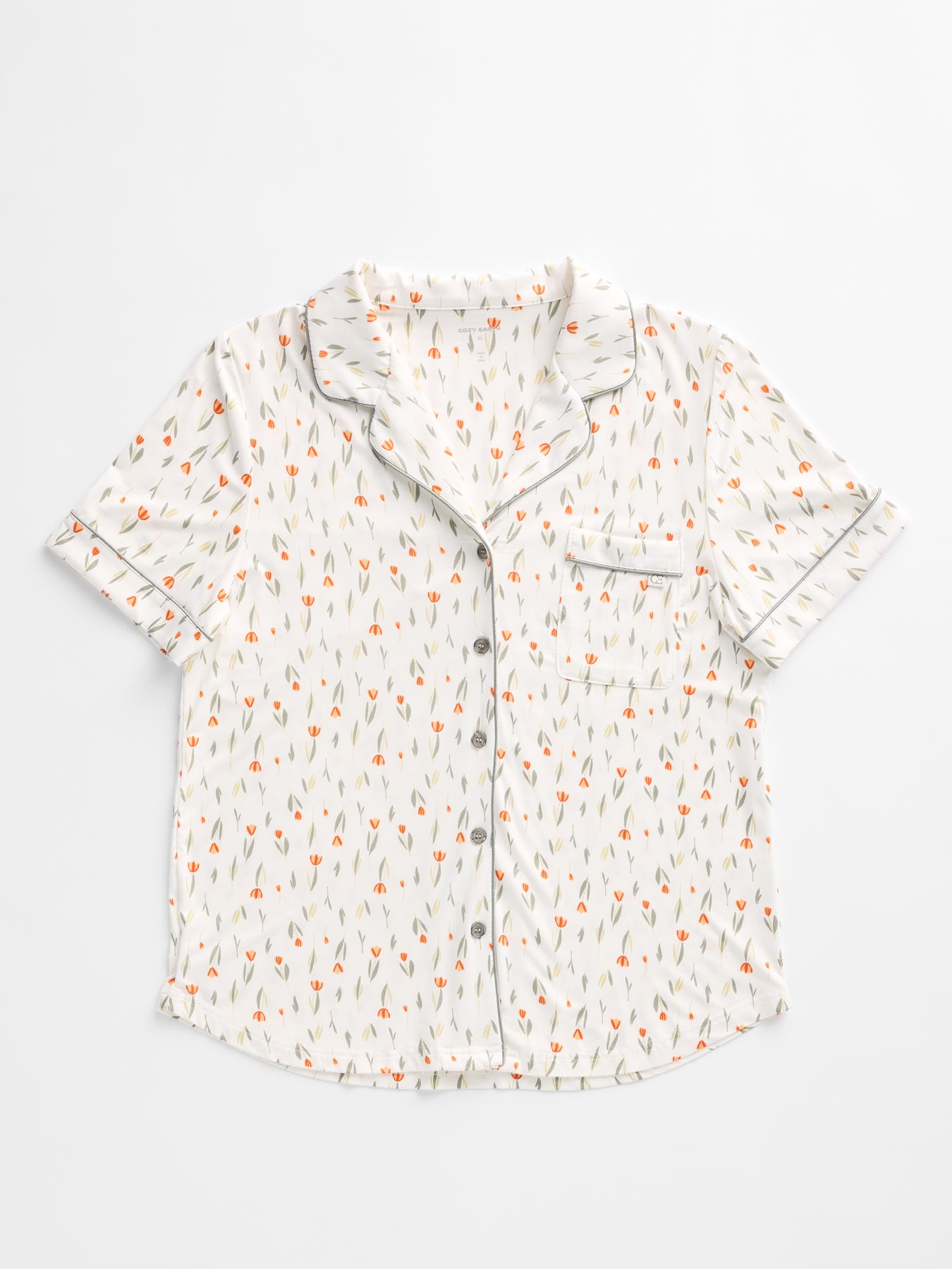 Cozy Earth's Women's Bamboo Stretch-Knit Short Sleeve Pajama Set features a white short-sleeved top with an orange and gray floral pattern, a notched collar, black piping, and a single breast pocket. 