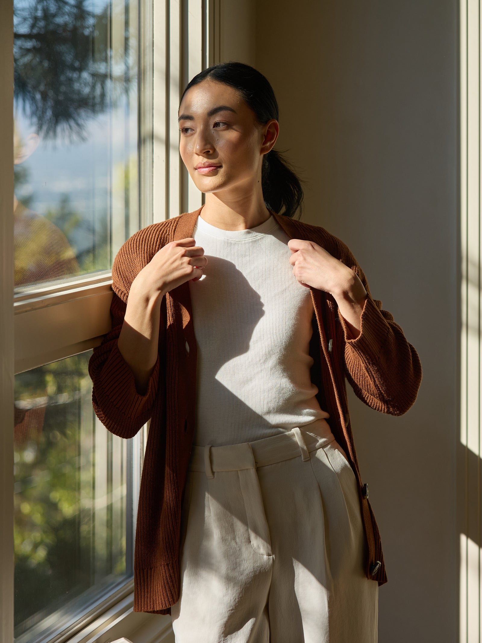 Woman wearing Oversized Classic Cardigan in Spice looks out a window. 