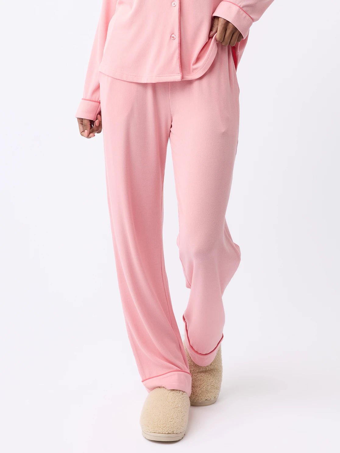 A woman is walking in Cozy Earth's Women's Bamboo Rib-Knit Classic Pajama Pant and matching button-up top, paired with beige fuzzy slippers against a plain white background. |Color:Tulip