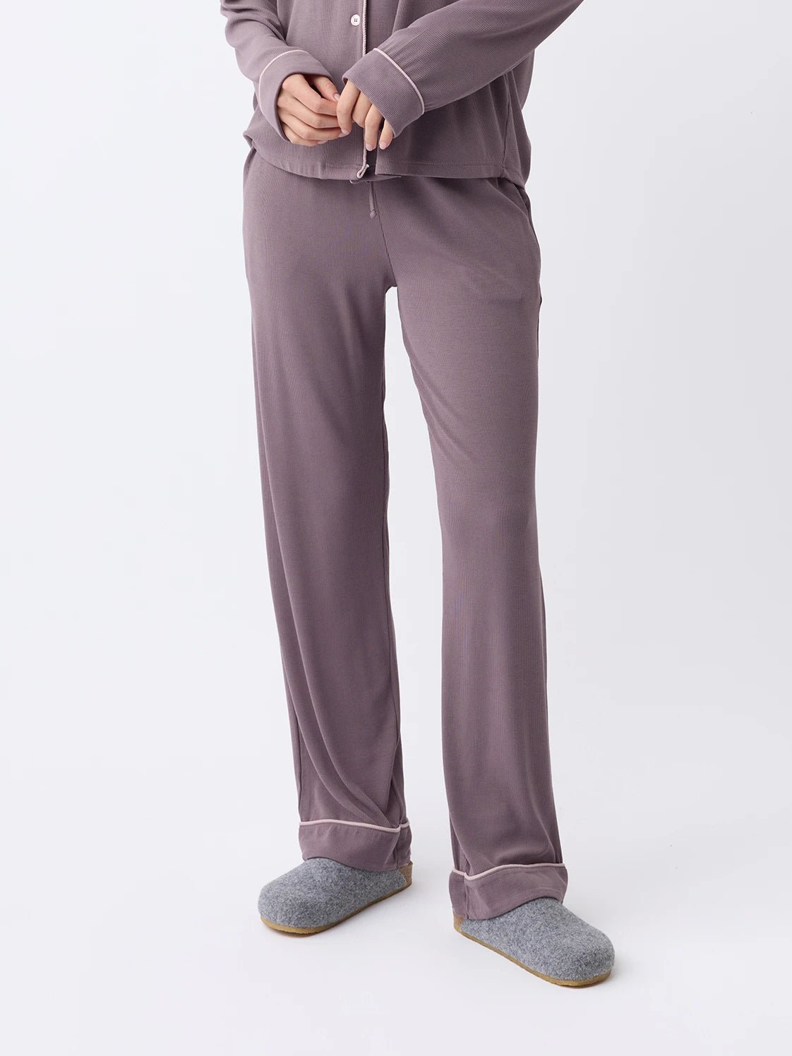 A woman dons a Cozy Earth mauve Women's Bamboo Rib-Knit Classic Pajama Pant with gray slippers against a plain backdrop. The long-sleeve, loose fit offers a comfortable, relaxed look. |Color:Twilight