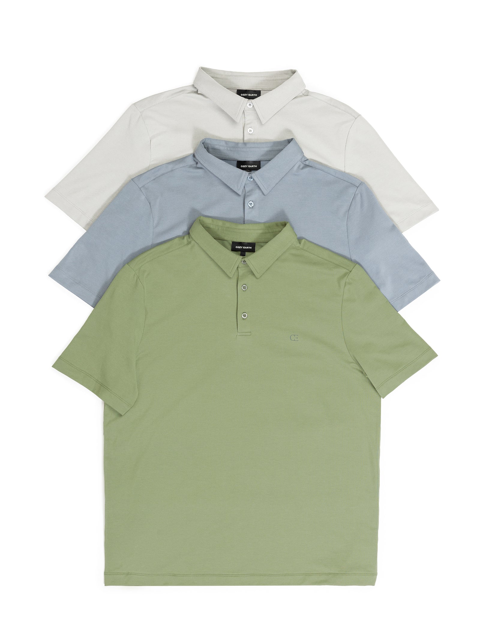 The Men's Everyday Polo shirts from Cozy Earth are stacked in a tiered formation with colors in beige, light blue, and olive green. Each shirt is neatly arranged, showcasing a collar and buttoned placket against a white background. 