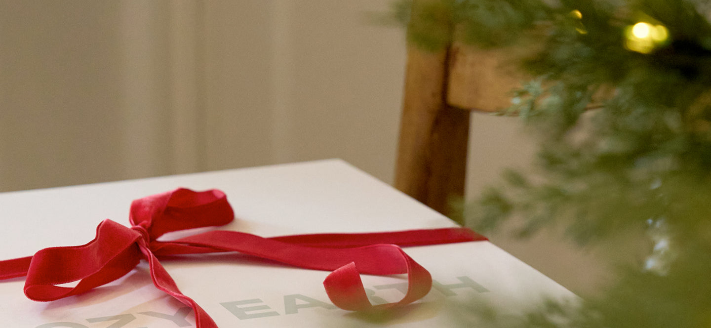 Gift box with a red ribbon on a table next to a Christmas tree.
