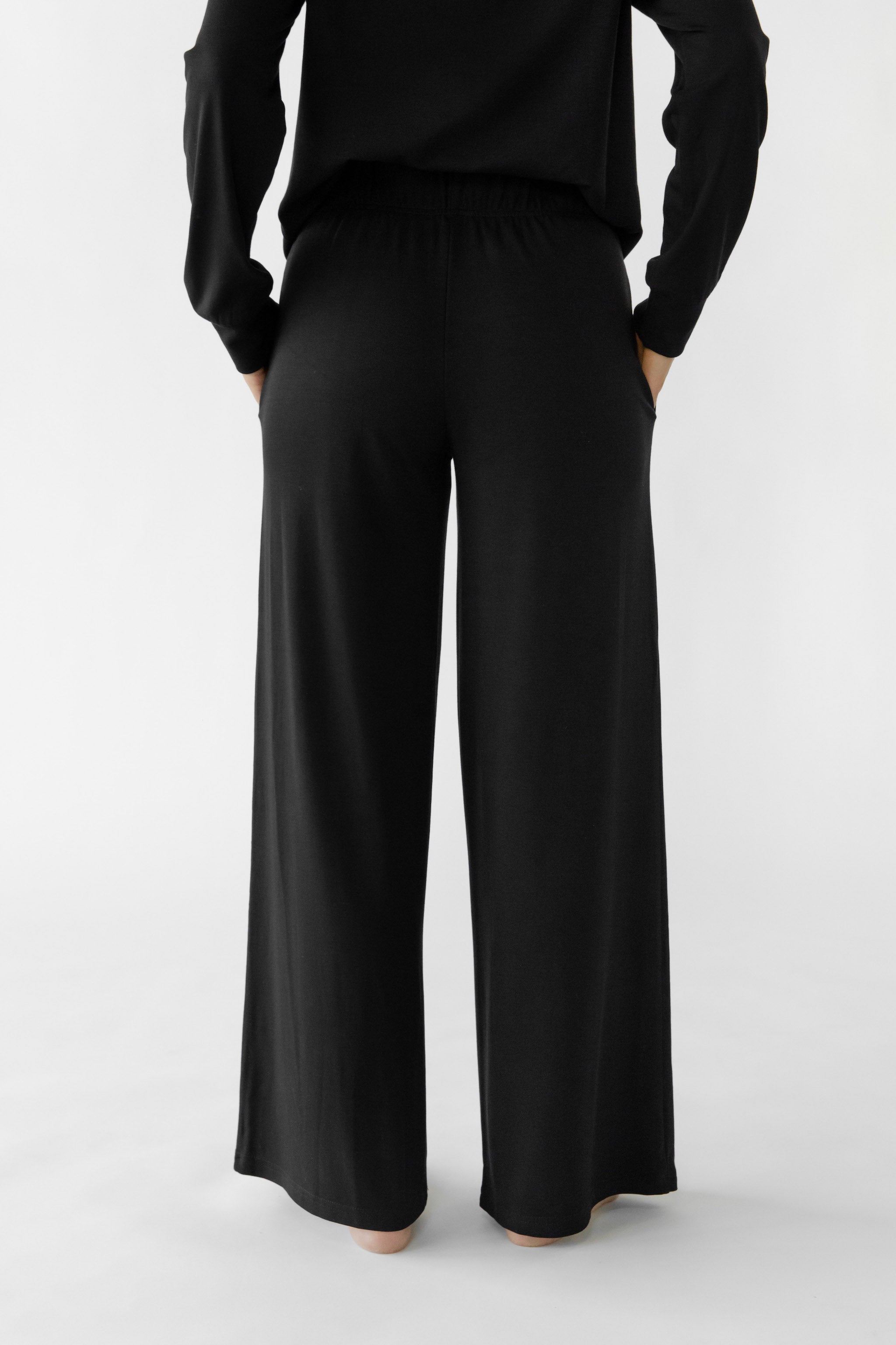 A person is wearing the Women's Ultra-Soft Bamboo Wide Leg Pull On Pant & Pullover Set by Cozy Earth, viewed from the back against a plain white background. |Color:Black