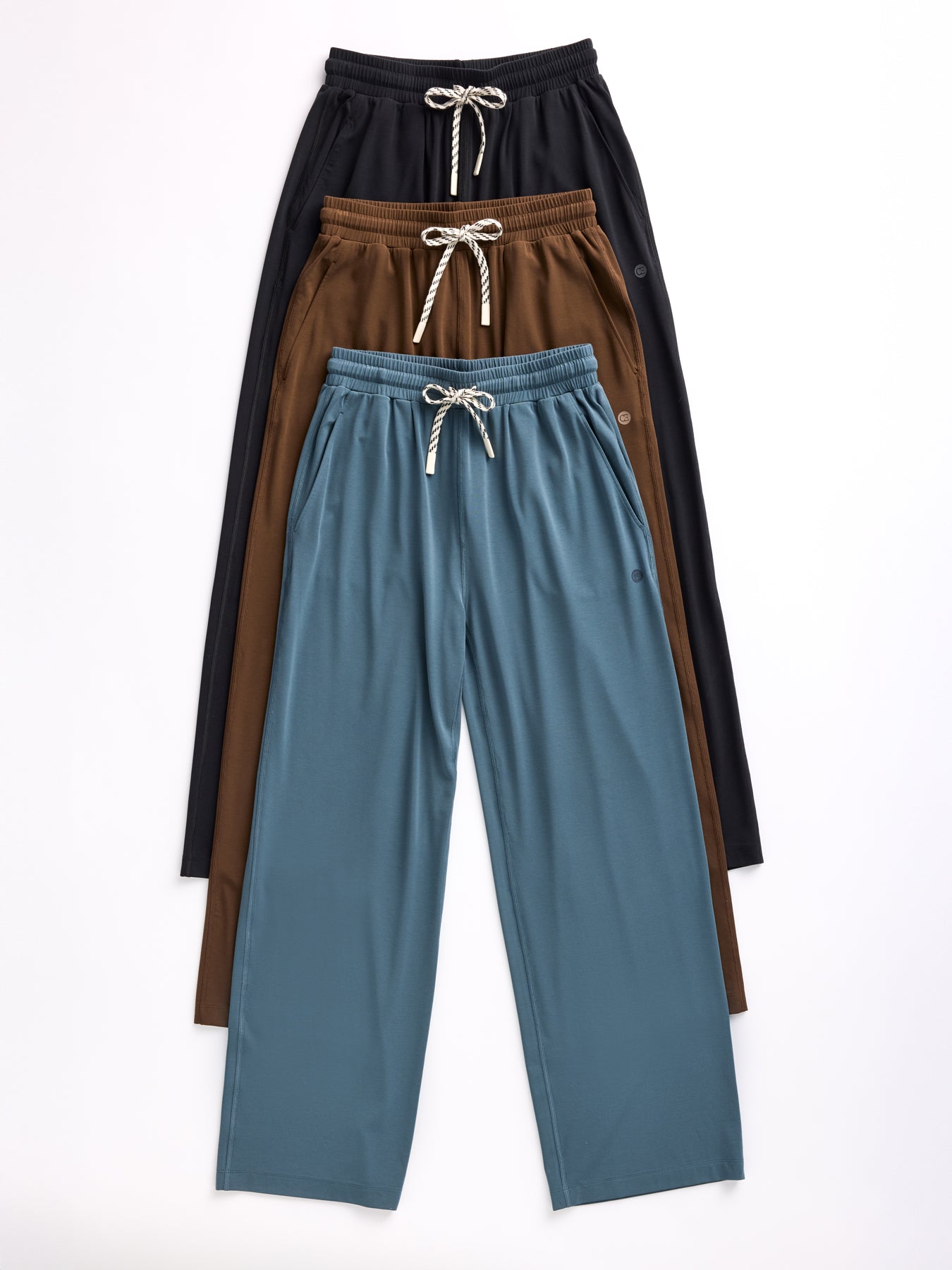 Three pairs of Cozy Earth's Women's Studio Wide Leg Pants with drawstring waistbands arranged vertically in black, brown, and teal. Crafted from a soft, flowing fabric. 