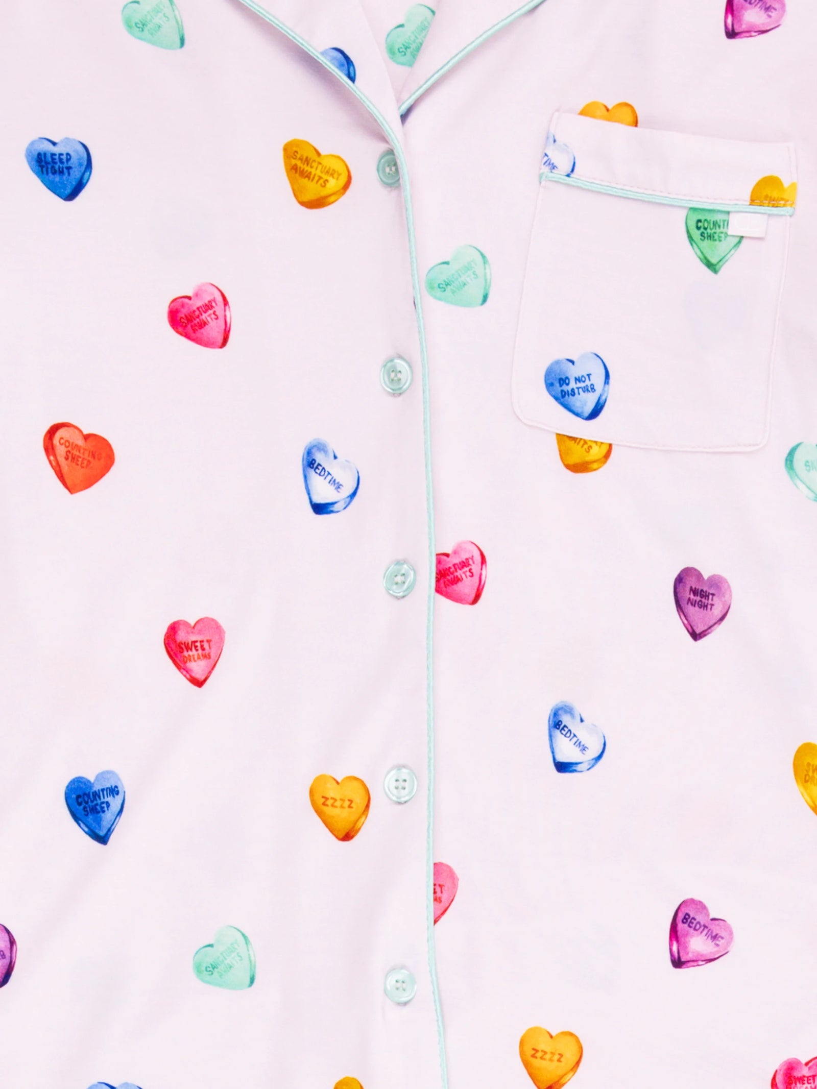 The Women's Long Sleeve Bamboo Pajama Top by Cozy Earth features a pastel design with multicolored heart motifs displaying messages like "KEEP SWEET" and "COZY VIBES." It includes front buttons and an upper left pocket. 