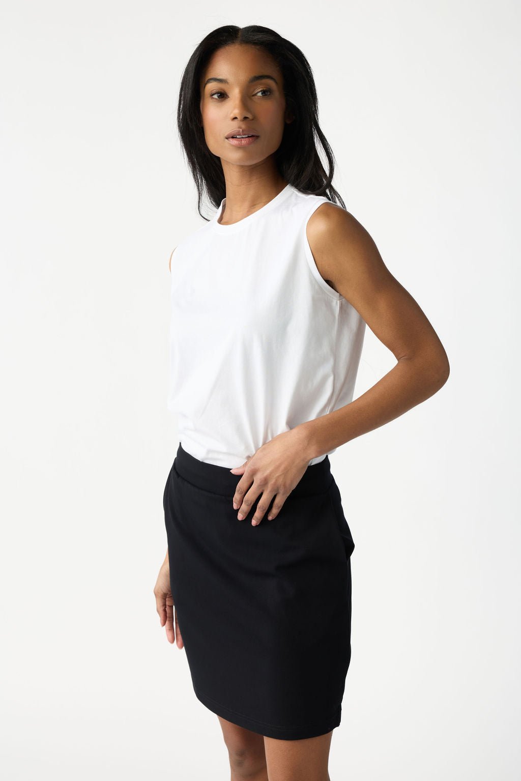 A woman with dark hair wears Cozy Earth Women's All Day Sleeveless Tee in White. She's shown from the hips up in front of a white background. 
