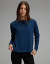 A person with long brown hair is wearing the Cozy Earth Women’s All Day Long Sleeve Tee in navy blue and black pants, standing against a plain gray background and looking at the camera.|Color:Obsidian