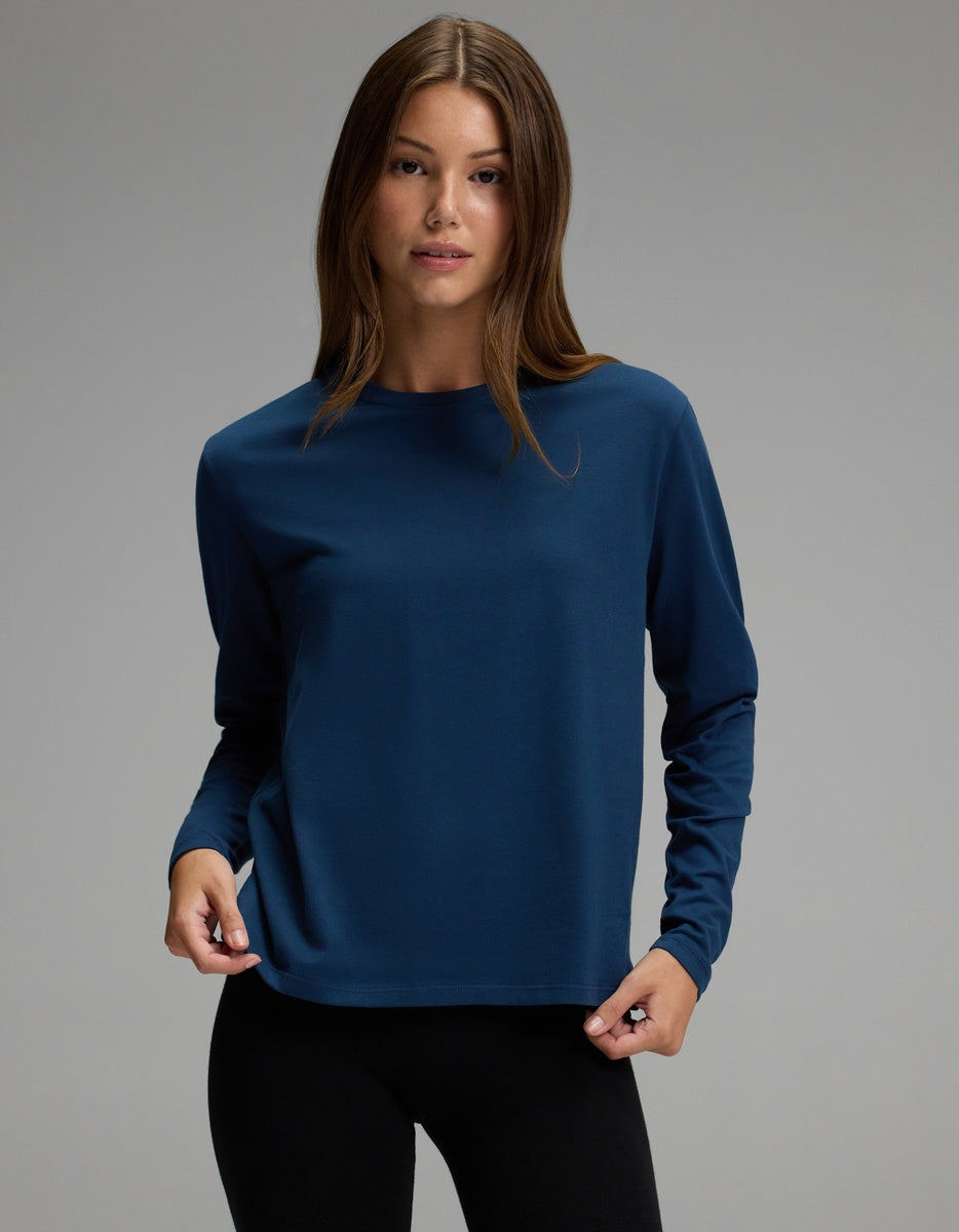 A person with long brown hair is wearing the Cozy Earth Women’s All Day Long Sleeve Tee in navy blue and black pants, standing against a plain gray background and looking at the camera.|Color:Obsidian