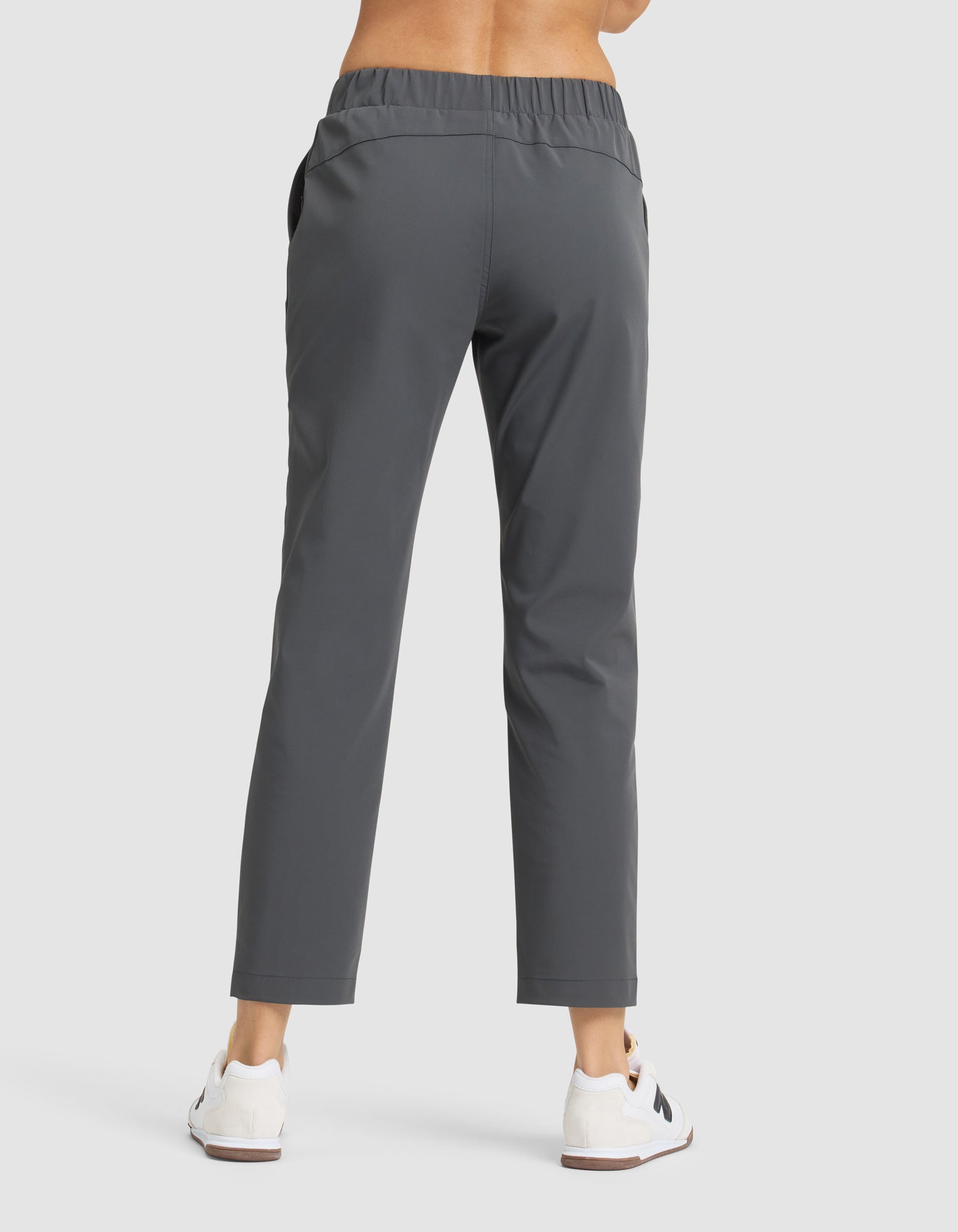 A person faces away, wearing Cozy Earth's Women's Always Cropped Pant in gray with an elastic waistband, paired with white sneakers on a plain light background. 