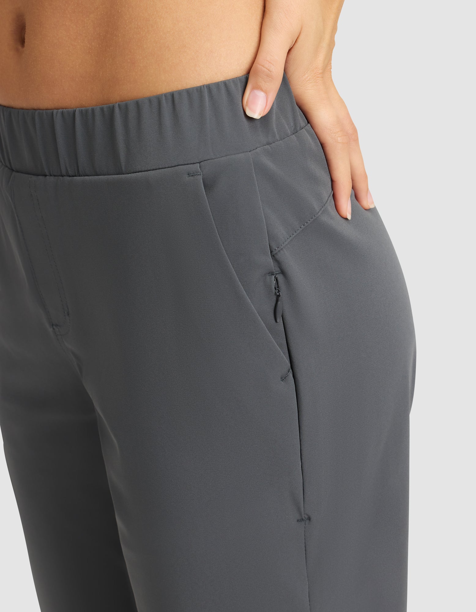 A close-up of a woman wearing Cozy Earth's Women's Always Cropped Pant in gray, featuring an elastic waistband and front pocket, with her left hand in the pocket against a plain light gray background. 