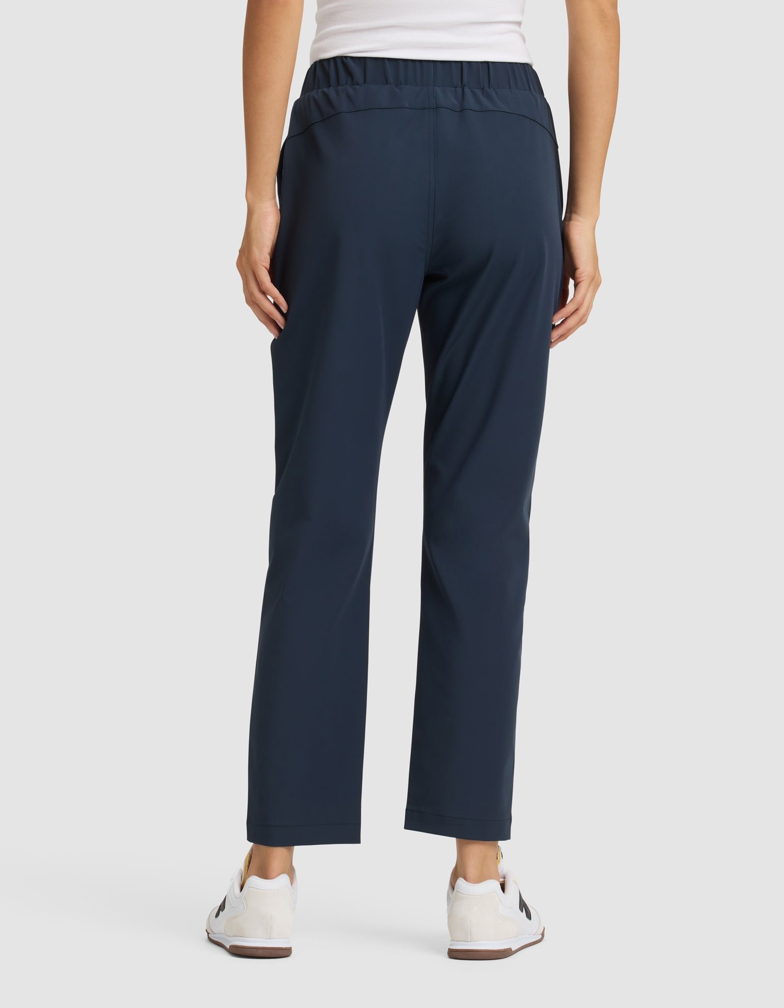 A person faces away, wearing Cozy Earth Women's Always Cropped Pant in navy blue, a white sleeveless top, and white sneakers against a plain light background. |Color:Eclipse