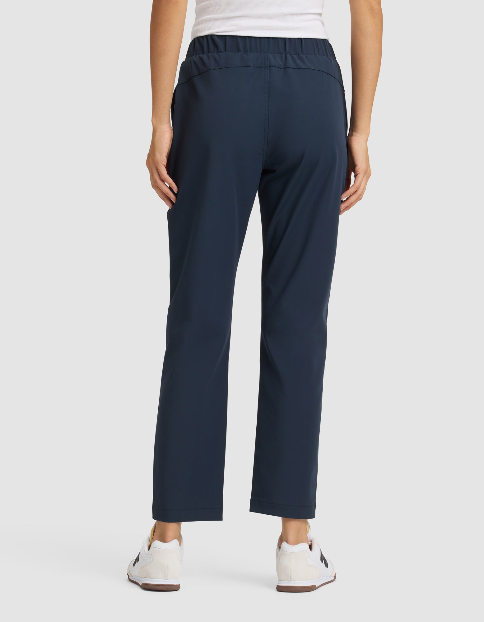 A person faces away, wearing Cozy Earth Women's Always Cropped Pant in navy blue, a white sleeveless top, and white sneakers against a plain light background. |Color:Eclipse