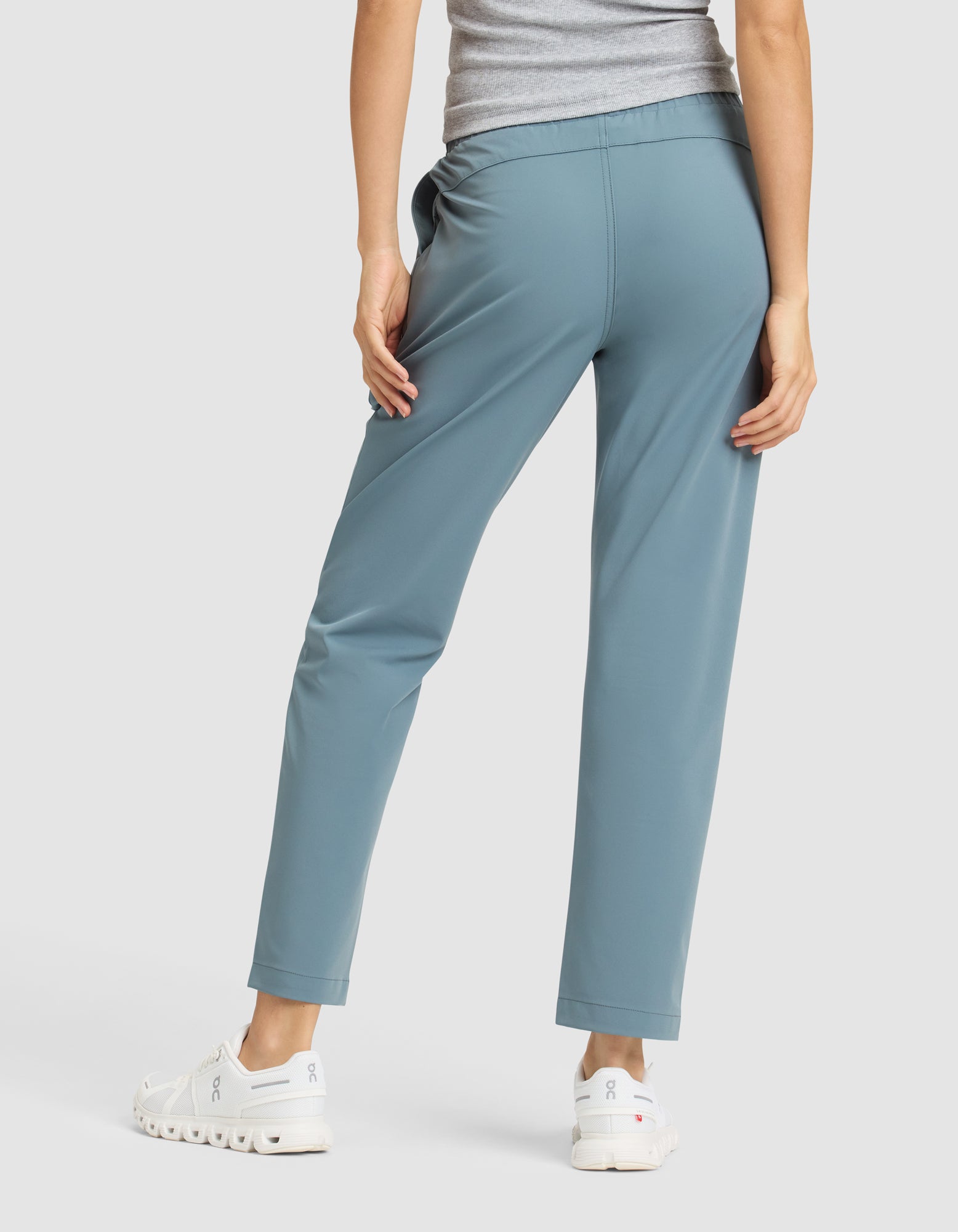 A woman, shown from the back, stands against a plain white background wearing the Cozy Earth Women's Always Cropped Pant in light blue, paired with a gray top and white sneakers. 