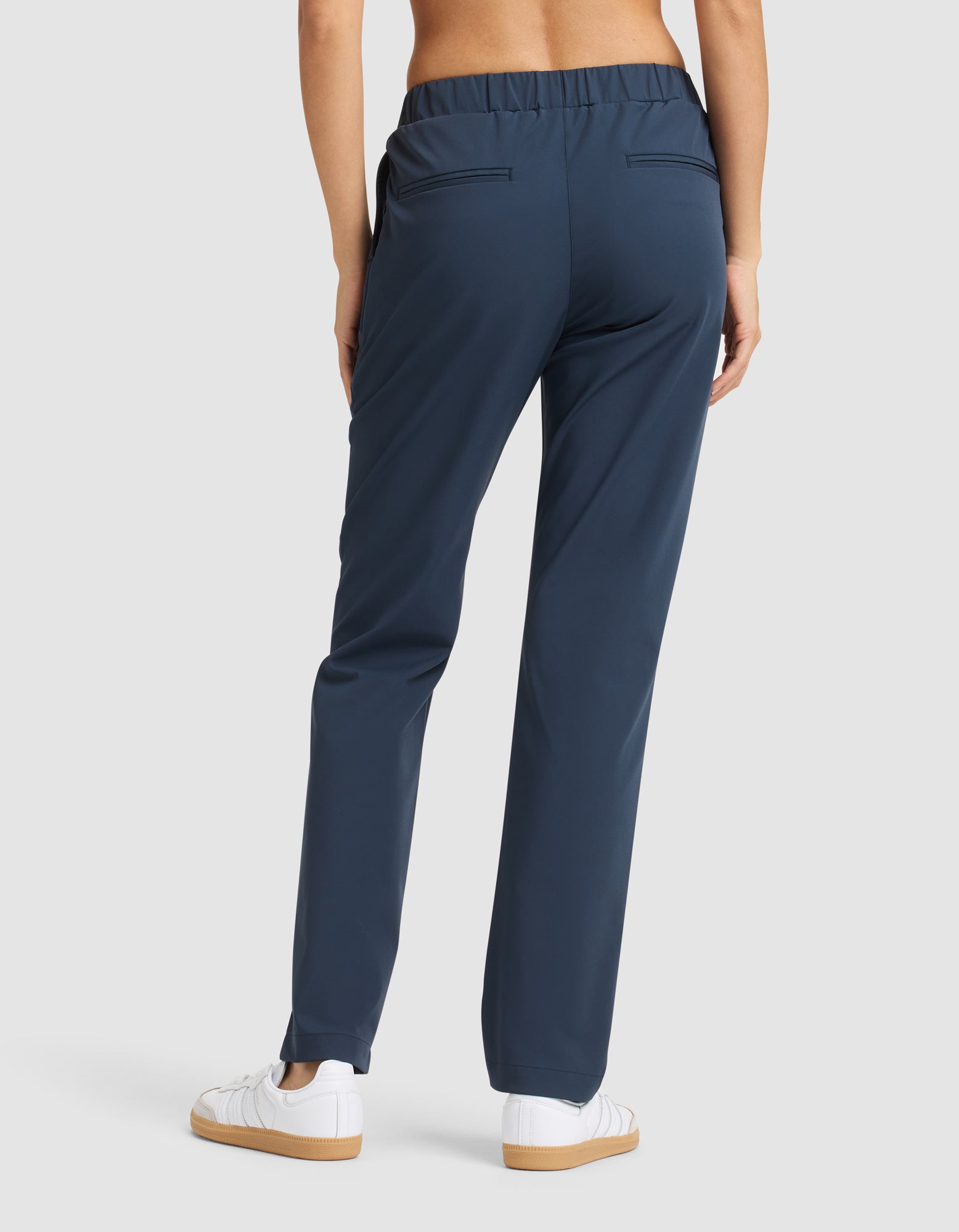 A woman is seen from the back wearing Cozy Earth’s Women's Always Pant in navy blue and white sneakers, standing against a plain light gray background. |Color:Eclipse