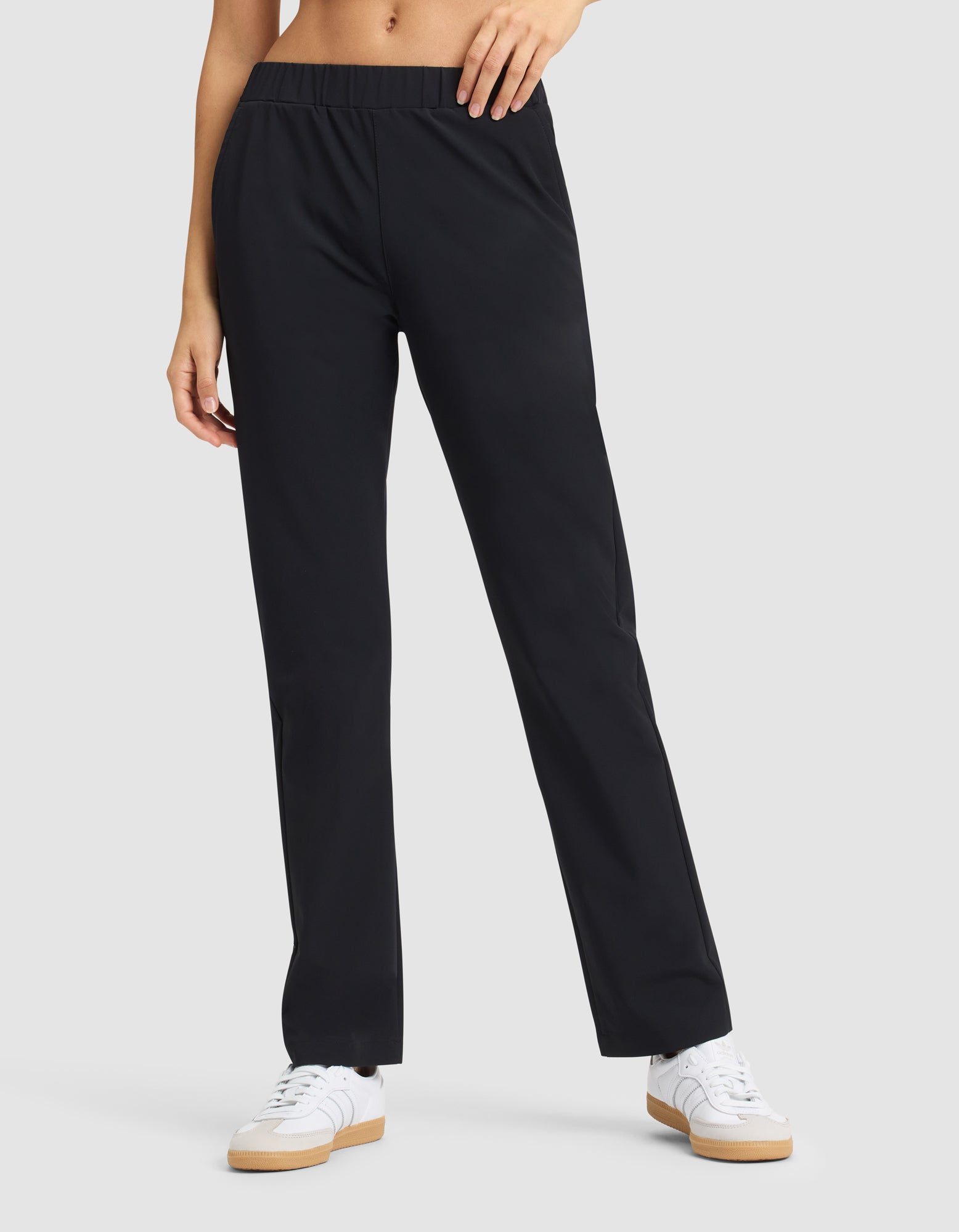 A woman models the Cozy Earth Women's Always Pant in black with white sneakers, standing against a plain light gray background; only her lower torso and legs are shown. |Color:Jet Black