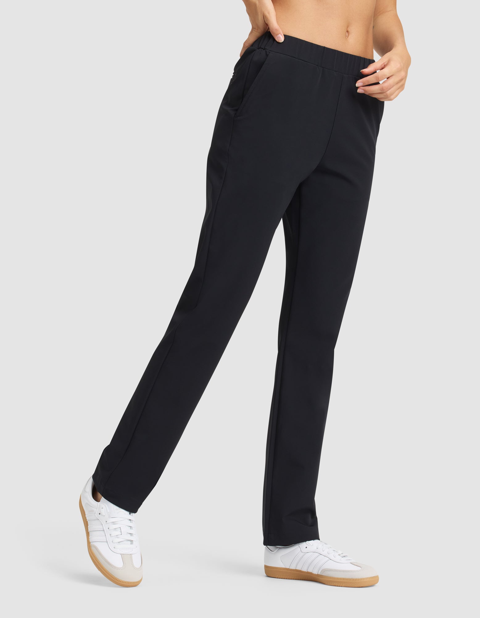 A person wearing Cozy Earth's Women's Always Pant in black and white sneakers, standing with one hand in their pocket against a plain light gray background. 