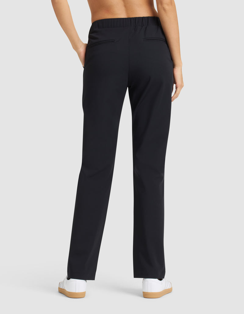 A person is shown from the back wearing Cozy Earth Women’s Always Pant in black with white sneakers, hands in pockets, against a plain light gray background.