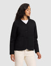 A woman stands against a plain background wearing the Cozy Earth Women's Andie Quilted Jacket in black, paired with a white shirt and off-white pants. She looks to the side with her arms relaxed at her sides.|Color:Jet Black