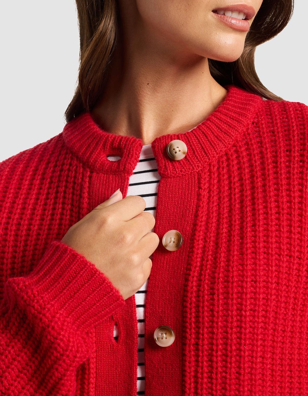 A woman wears the Cozy Earth Women's Arden Cardigan in textured red with tan buttons over a white and black striped shirt, shown from shoulders to mid-chest, with her hand near the collar.