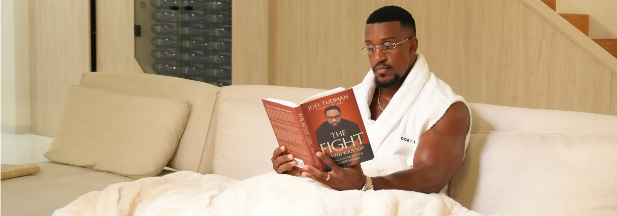 Ashton Hall reading a book on a sofa in a luxurious setting