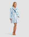 A person stands barefoot in the Cozy Earth Classic Stripe Resort Robe, featuring light blue and white stripes, a belted waist, and two large front pockets, set against a plain light gray background.|Color:Lake Stripe