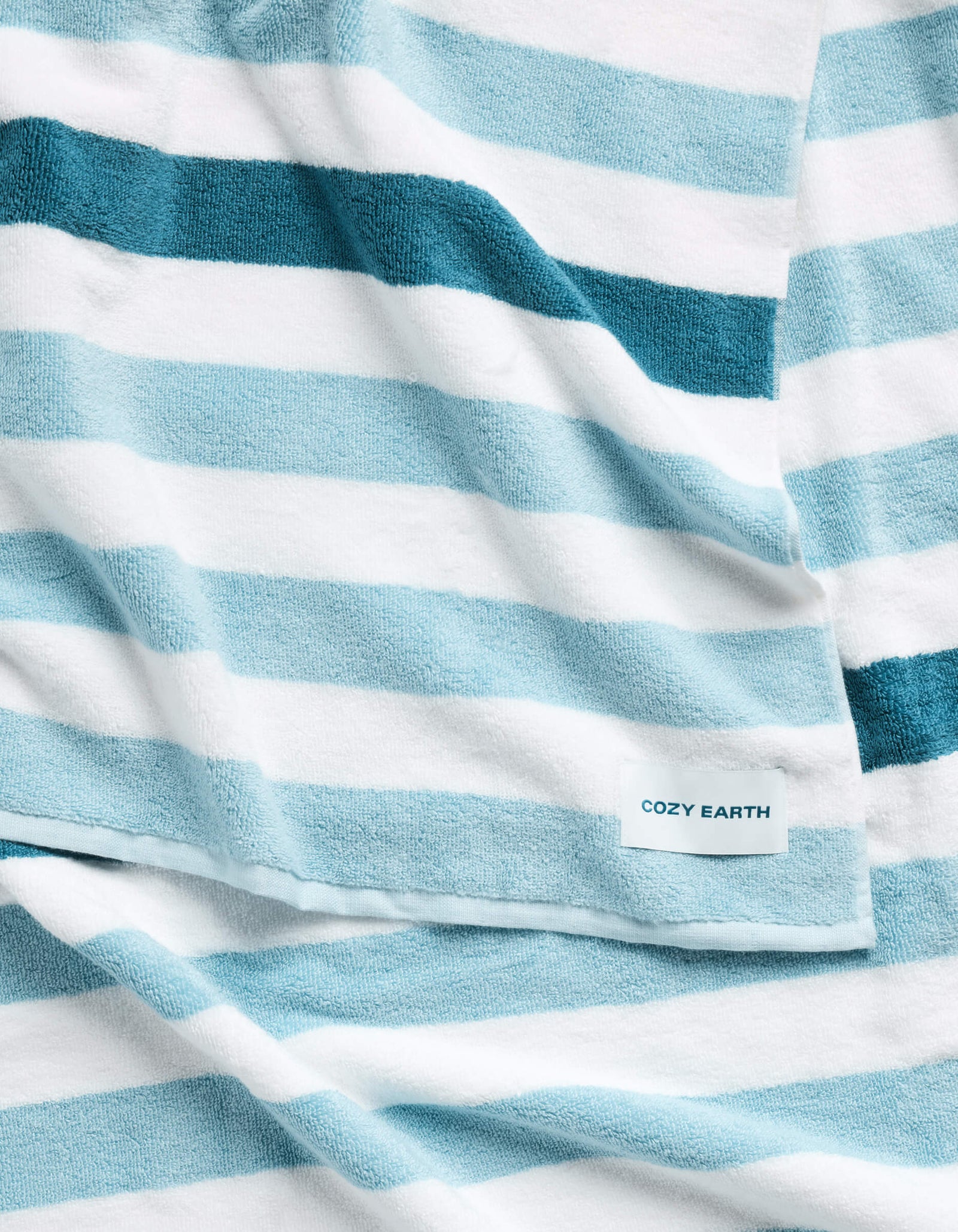The Classic Stripe Resort Towel by Cozy Earth is a soft towel with wide blue and white horizontal stripes, featuring a small label that reads "Cozy Earth.