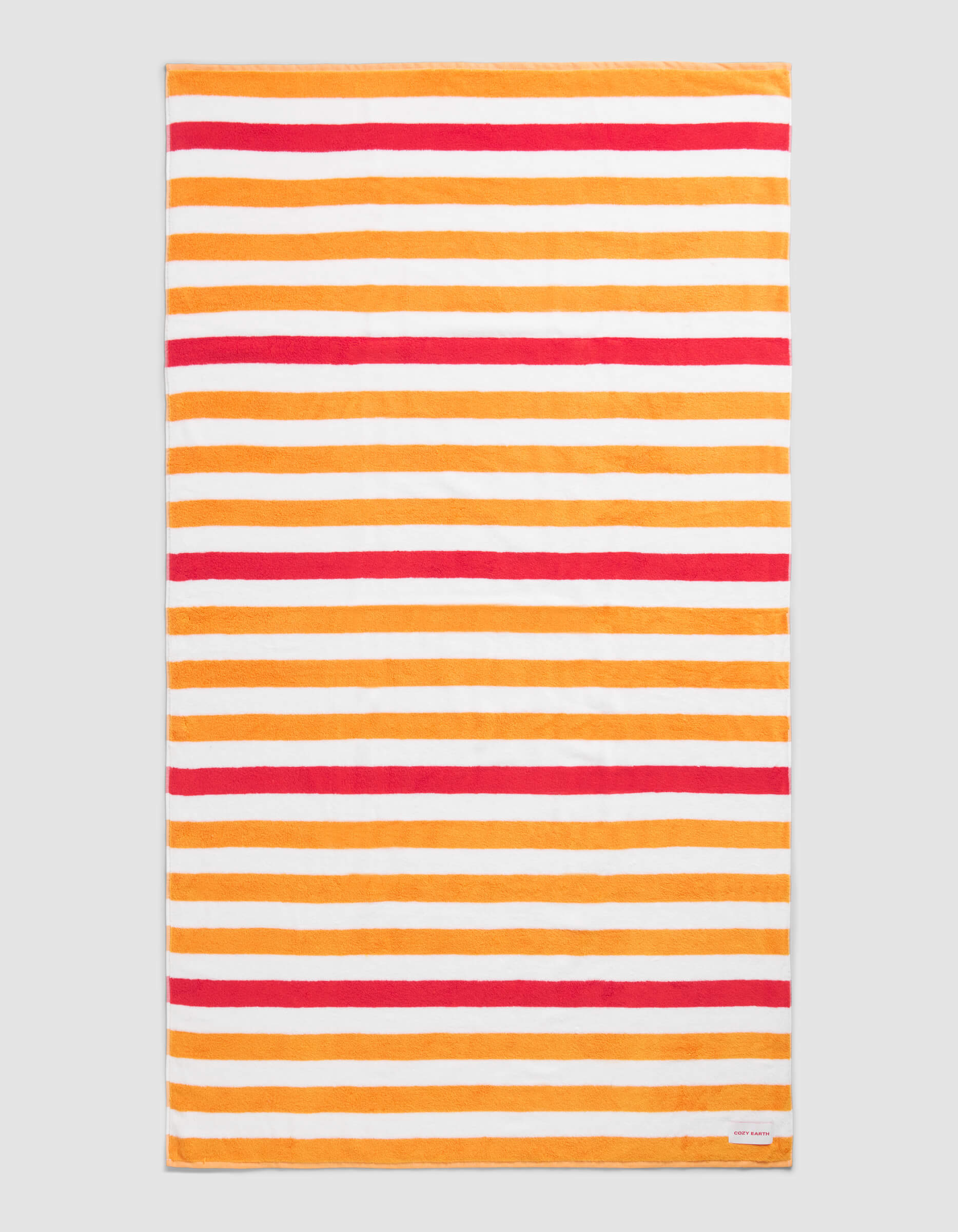 The Cozy Earth Classic Stripe Resort Towel in Mandarin Stripe features a rectangular design with horizontal orange, red, and white stripes of varying thickness on a neutral background and includes a small white corner tag.