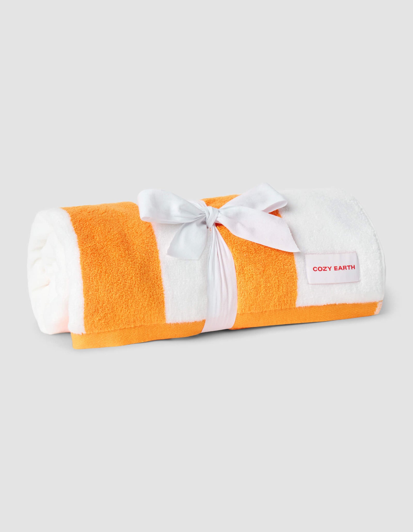 A rolled Classic Stripe Resort Towel by Cozy Earth, featuring orange and white stripes, is tied with a white ribbon and displayed on a plain light gray background.