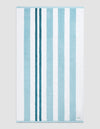 The Classic Stripe Resort Towel by Cozy Earth in Wave Stripe is shown laid flat on a light gray background. Alternating vertical blue and white stripes and a small white label in the bottom right corner are visible.|Color:Wave Stripe