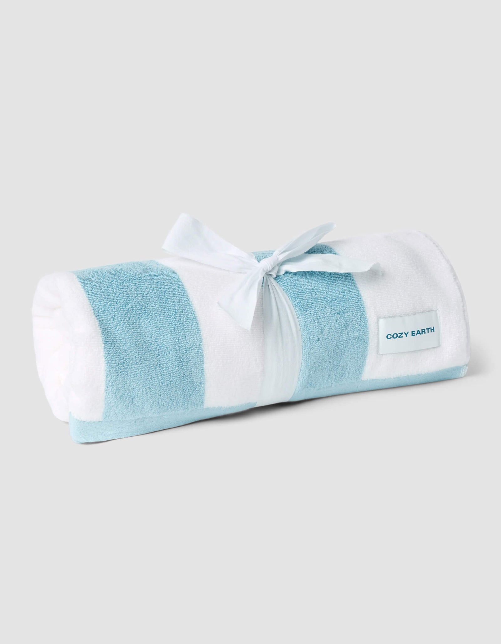 The Cozy Earth Classic Stripe Resort Towel, featuring light blue and white stripes and tied with a white ribbon, is displayed on a light gray background with a "COZY EARTH" tag.