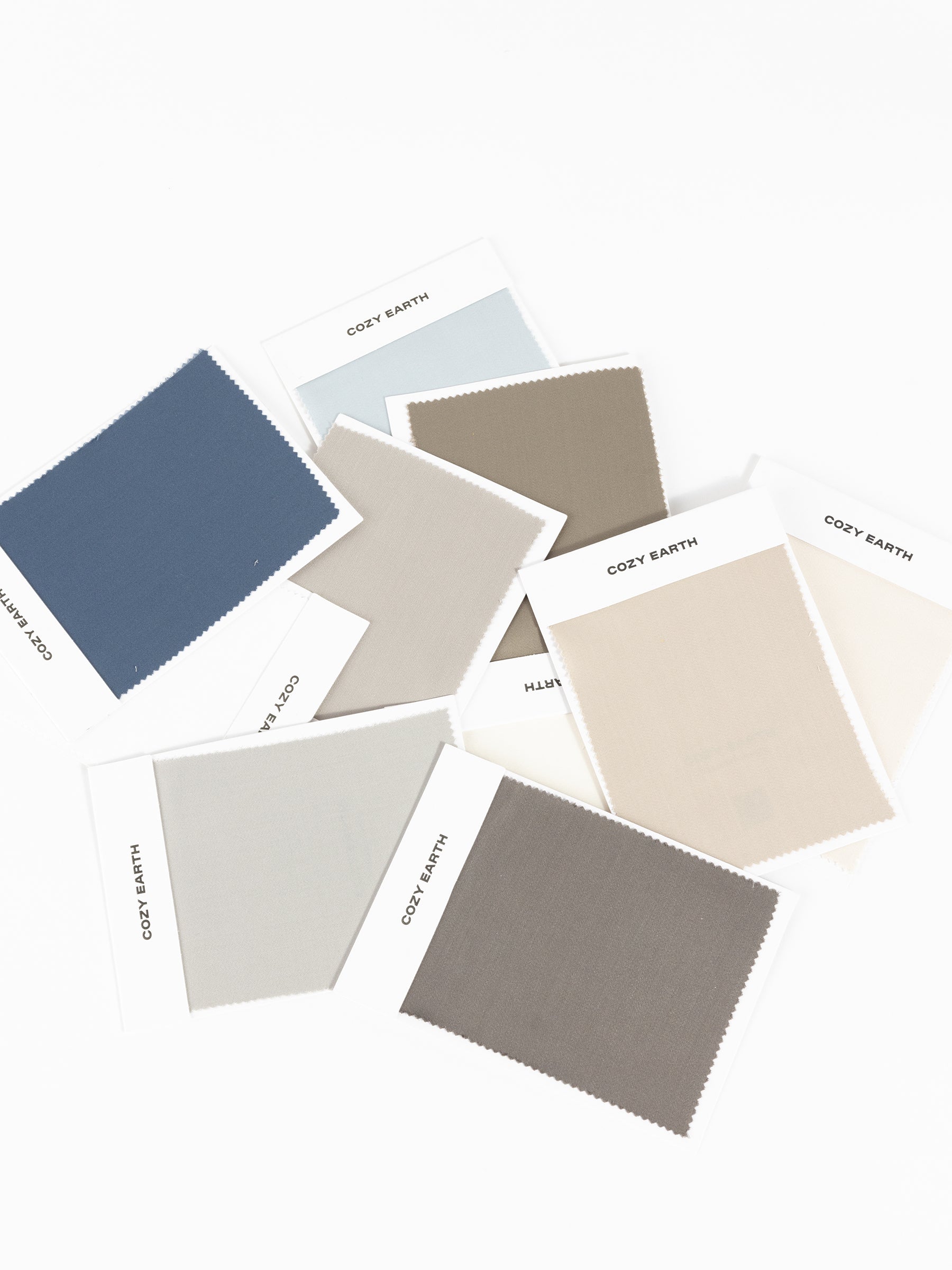 A set of Bamboo Sheet Swatches from the brand Cozy Earth, featuring a zigzag edge pattern, is displayed in an assortment of colors like blue, green, beige, and brown on a plain background.