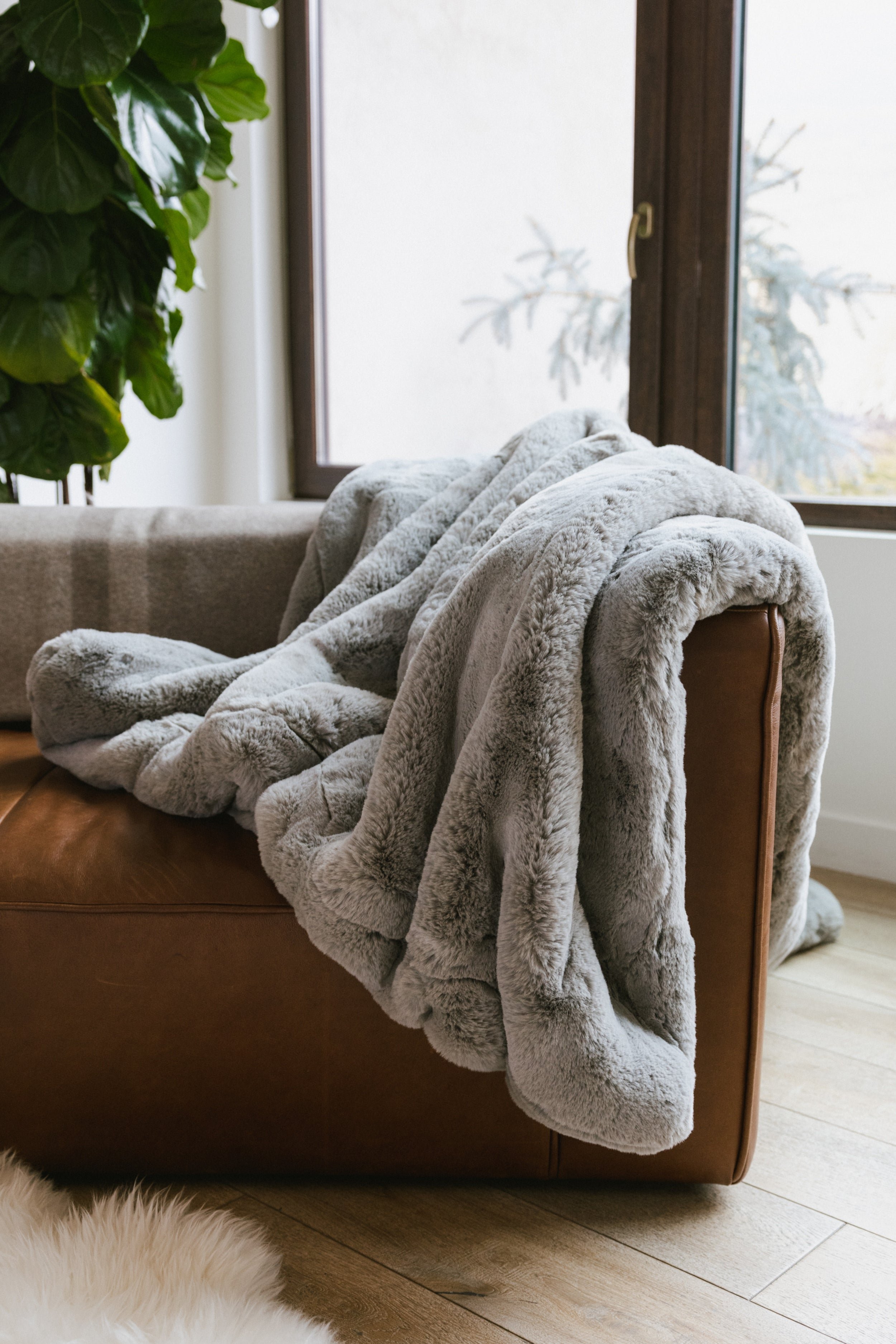 Dove Grey Oversized Throw Cuddle Blanket draped over couch next to window 