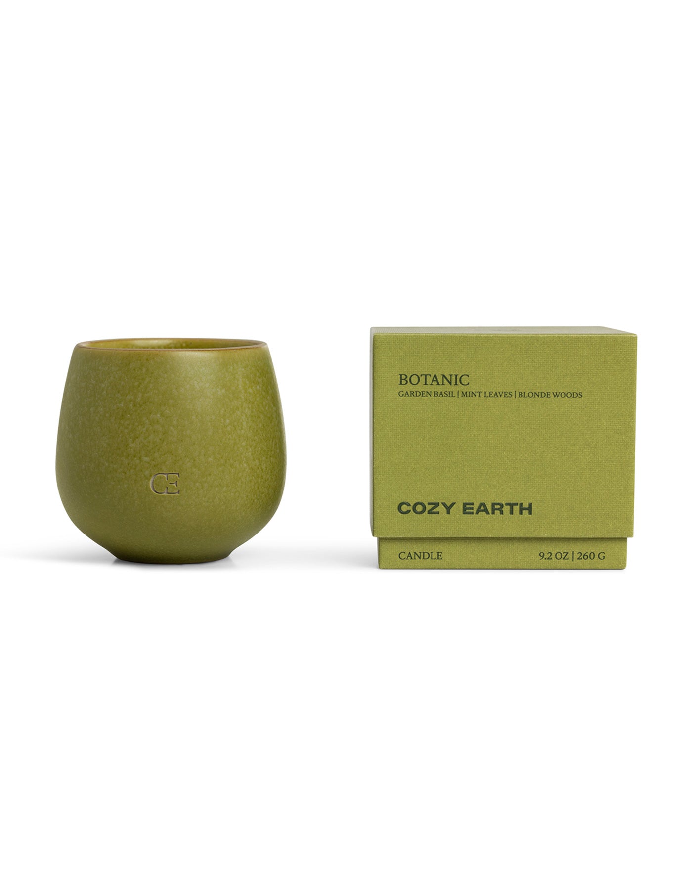 A green ceramic Candle BOTANIC by Cozy Earth sits beside its matching box, labeled with "garden basil, mint leaves, blonde woods" and "9.2 OZ 