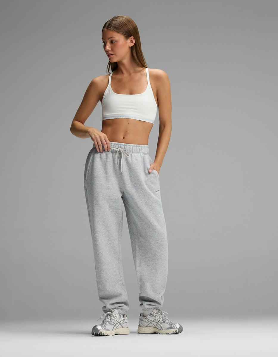 A woman wearing a white Cozy Earth Women’s Balance Bra, grey sweatpants, and athletic sneakers.