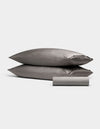 The Bamboo Bedding Basic Bundle by Cozy Earth, featuring two gray pillows stacked and a folded gray bedsheet in front, is showcased against a plain white background.|Color:Charcoal
