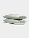 The Cozy Earth Bamboo Bedding Basic Bundle features two light gray pillows stacked together with a matching pillowcase rolled in front, all displayed against a plain white background.|Color:Laurel