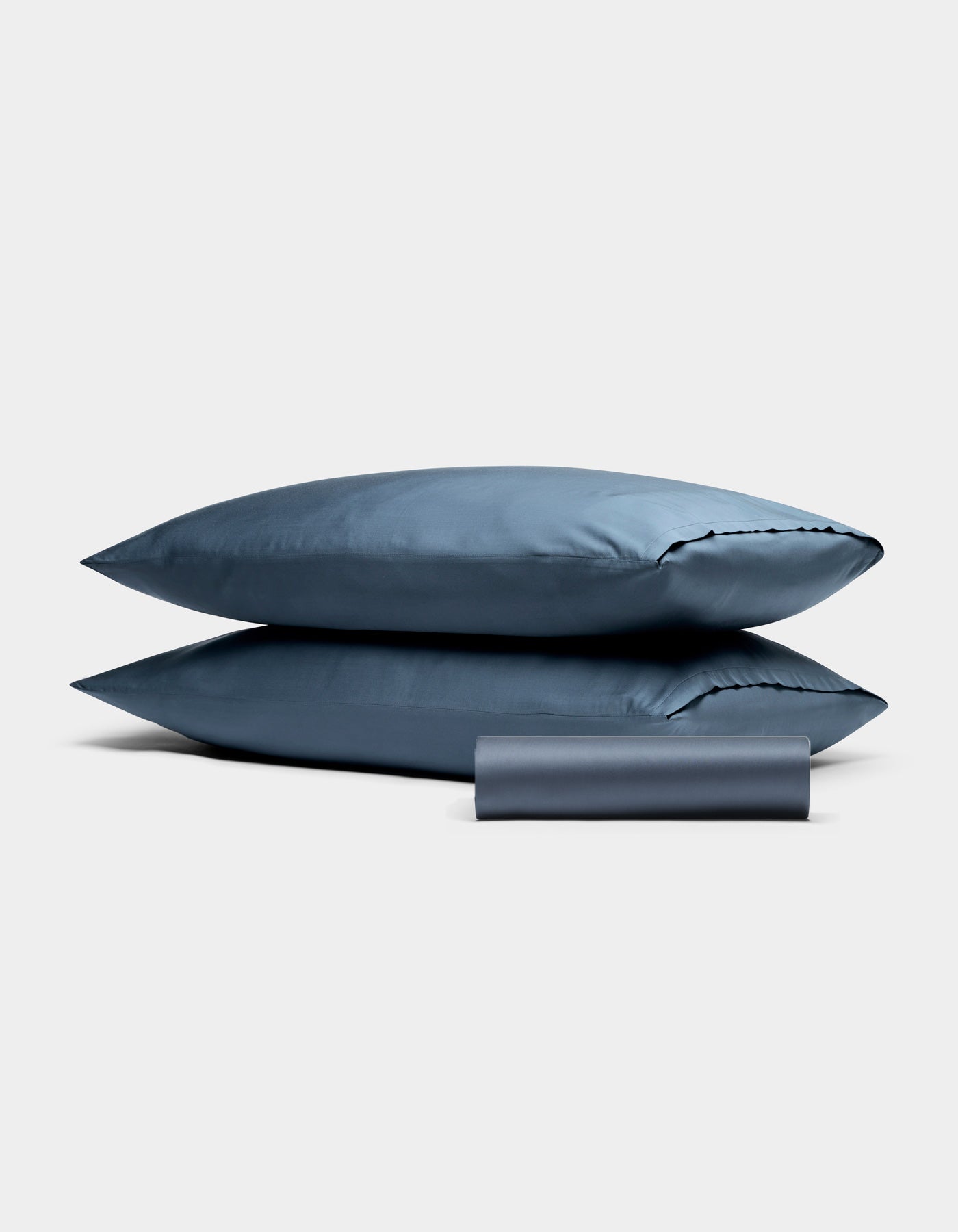 Cozy Earth Bamboo Bedding Basic Bundle: two stacked blue pillows with a matching rolled blue pillowcase on a plain light gray background.