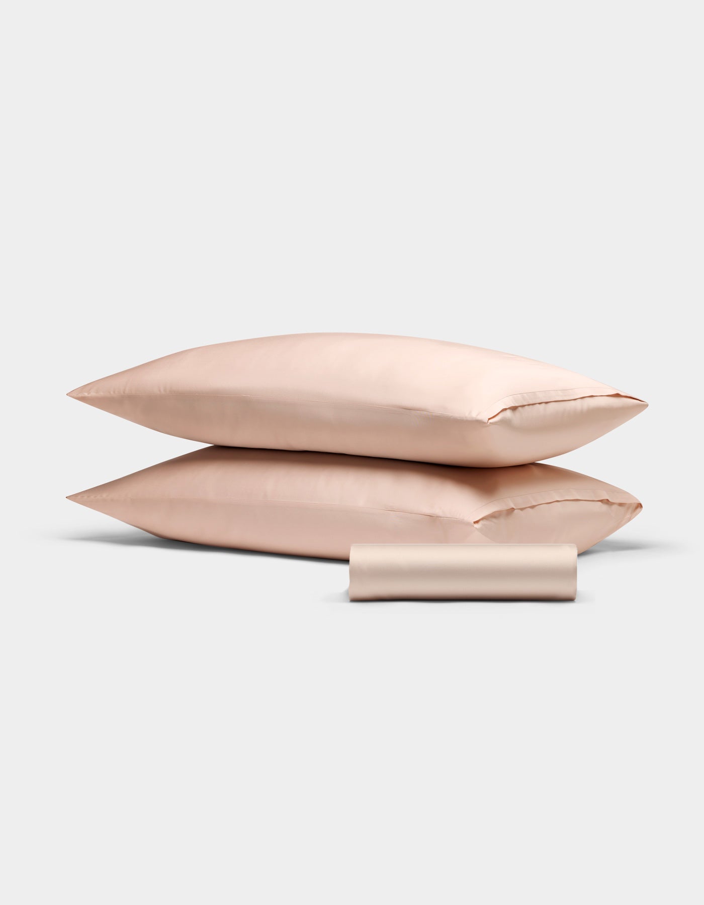 The Cozy Earth Bamboo Bedding Basic Bundle features two light pink satin pillowcases stacked, with a matching satin sleep mask in front, all set against a plain white background.|Color:Peony