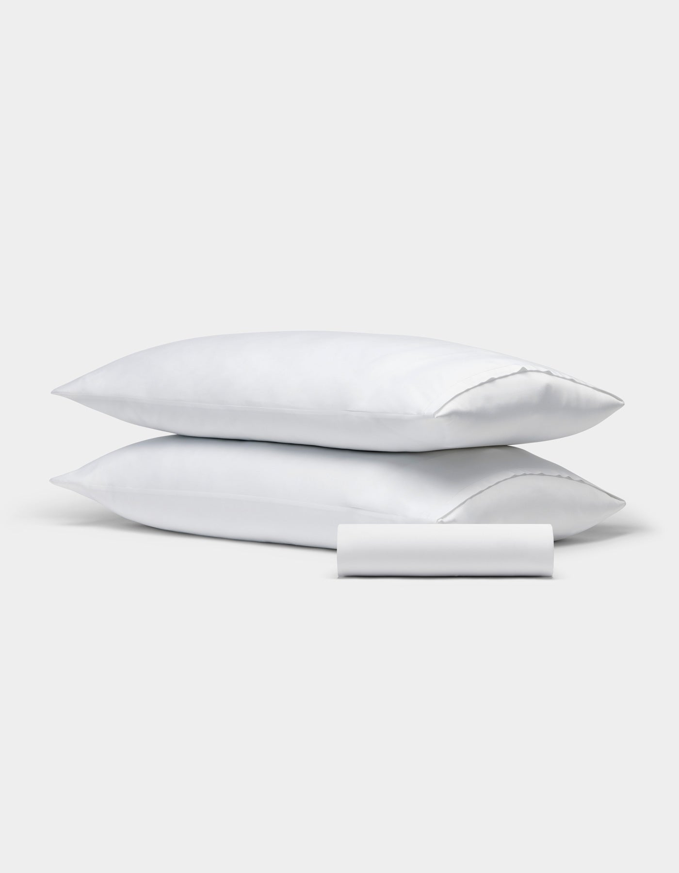 Two white rectangular pillows from the Cozy Earth Bamboo Bedding Basic Bundle are stacked, with a matching small cylindrical bolster in front, all set against a plain light gray background.
