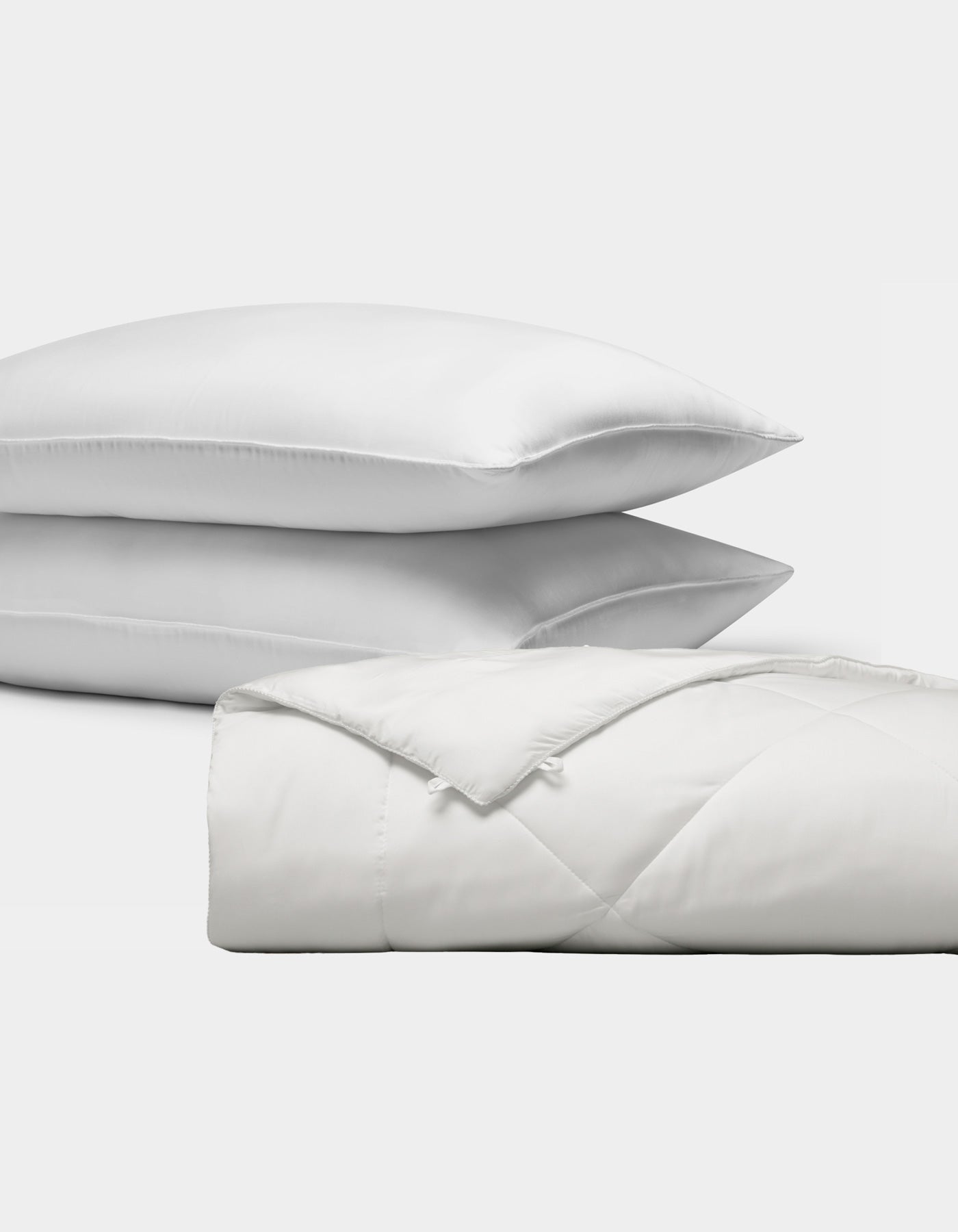 The Bamboo Insert Bundle by Cozy Earth features two stacked white pillows and a folded, quilted white comforter, all displayed against a plain white background.